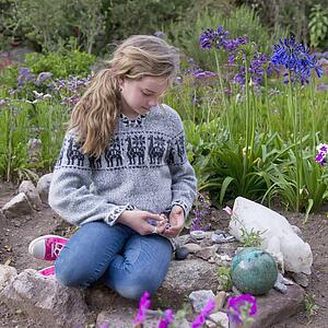 A Girls Sits On Stones By A Flower Garden At The Willka T'ika Guesthouse; Peru