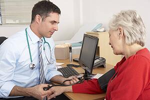 British doctor taking senior woman's blood pressure