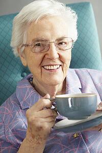 Senior Woman Relaxing In Chair With Hot Drink