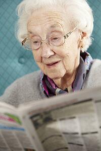 Senior Woman Relaxing In Chair Reading Newspaper