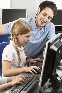 Teacher helping girl using computer in class