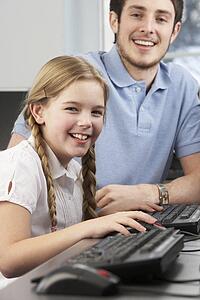 Teacher helping girl using computer in class