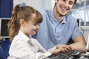 Teacher helping girl using computer in class