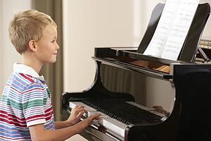 Young boy playing grand piano at home