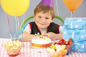 Young boy with birthday cake and gifts at party
