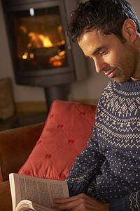 Middle Aged Man Relaxing With Book By Cosy Log Fire