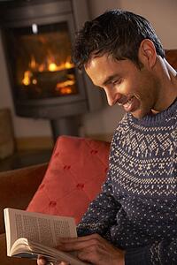 Middle Aged Man Relaxing With Book By Cosy Log Fire
