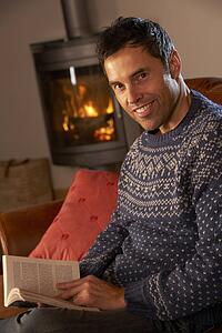 Middle Aged Man Relaxing With Book By Cosy Log Fire