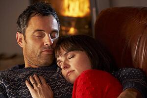 Middle Aged Couple Cuddling On Sofa By Cosy Log Fire