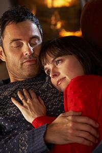 Middle Aged Couple Cuddling On Sofa By Cosy Log Fire