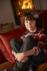 Young Boy Sitting On Sofa By Cosy Log Fire