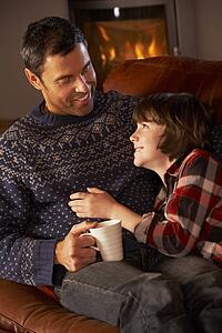 Father And Son Relaxing With Hot Drink By Cosy Log Fire