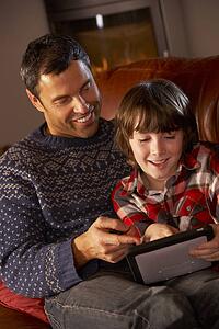 Father And Son Using Tablet Computer By Cosy Log Fire