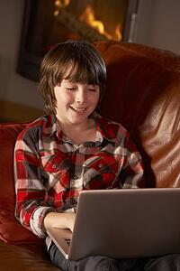 Young Boy Relaxing With Laptop By Cosy Log Fire