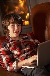 Young Boy Relaxing With Laptop By Cosy Log Fire
