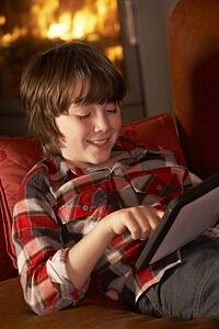Young Boy Relaxing With Tablet Computer By Cosy Log Fire