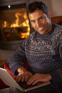 Middle Aged Man Using Laptop Computer By Cosy Log Fire