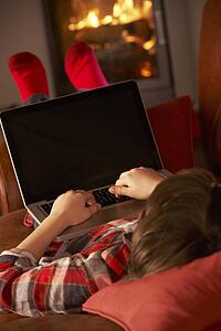 Young Boy Relaxing With Laptop By Cosy Log Fire