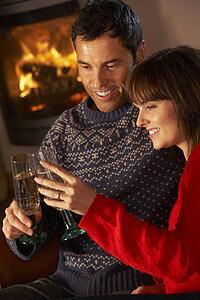 Middle Aged Couple Sitting Sofa By Cosy Log Fire With Glass Of Champagne