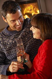 Middle Aged Couple Sitting Sofa By Cosy Log Fire With Glass Of Champagne