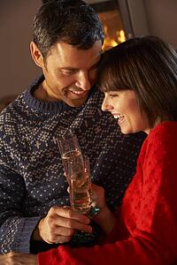 Middle Aged Couple Sitting Sofa By Cosy Log Fire With Glass Of Champagne