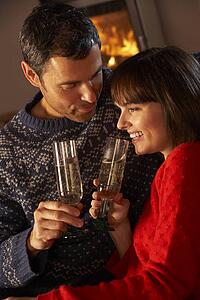 Middle Aged Couple Sitting Sofa By Cosy Log Fire With Glass Of Champagne