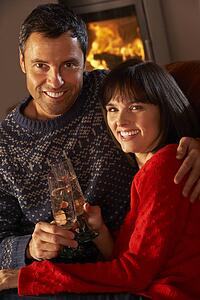 Middle Aged Couple Sitting Sofa By Cosy Log Fire With Glass Of Champagne