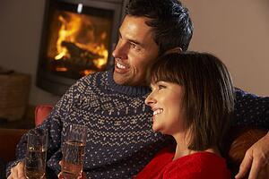 Middle Aged Couple Sitting Sofa By Cosy Log Fire With Glass Of Champagne