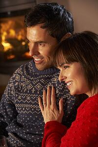 Middle Aged Couple Sitting Sofa Watching TV By Cosy Log Fire