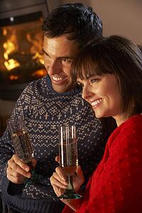 Middle Aged Couple Sitting Sofa By Cosy Log Fire With Glass Of Champagne