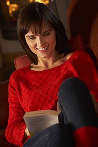 Middle Aged Woman Relaxing With Book By Cosy Log Fire