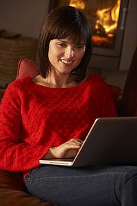 Middle Aged Woman Using Laptop Computer By Cosy Log Fire