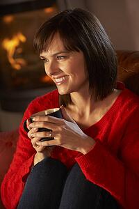 Middle Aged Woman Relaxing With Hot Drink By Cosy Log Fire