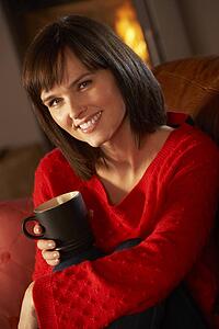 Middle Aged Woman Relaxing With Hot Drink By Cosy Log Fire