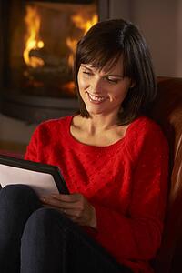 Middle Aged Woman Using Tablet Computer By Cosy Log Fire