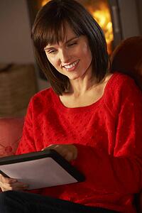 Middle Aged Woman Using Tablet Computer By Cosy Log Fire