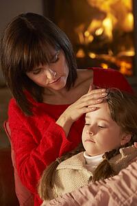 Mother Comforting Sick Daughter On Sofa By Cosy Log Fire