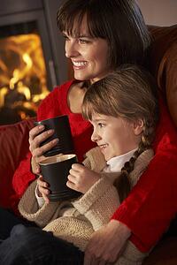 Mother And Daughter Relaxing With Hot Drink Watching TV By Cosy Log Fire