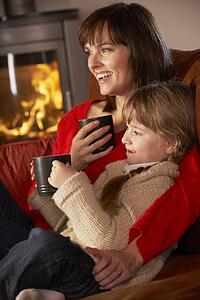 Mother And Daughter Relaxing With Hot Drink Watching TV By Cosy Log Fire