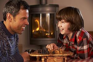 Father And Son Playing Chess By Cosy Log Fire