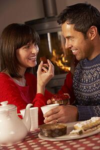 Couple Enjoying Tea And Cake By Cosy Log Fire