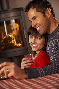 Middle Aged Couple Sitting On Sofa Watching TV By Cosy Log Fire