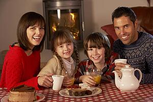 Portrait Of Family Enjoying Tea And Cake By Cosy Log Fire