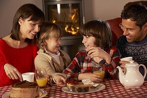 Portrait Of Family Enjoying Tea And Cake By Cosy Log Fire