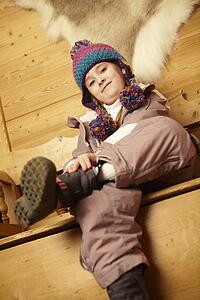 Young Girl Sitting On Wooden Seat Putting On Warm Outdoor Clothes And Boots