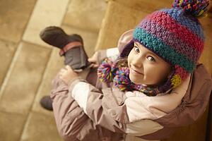 Young Girl Sitting On Wooden Seat Putting On Warm Outdoor Clothes And Boots