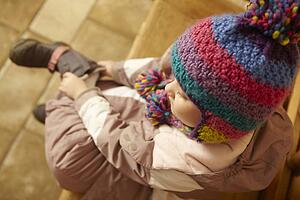 Young Girl Sitting On Wooden Seat Putting On Warm Outdoor Clothes And Boots