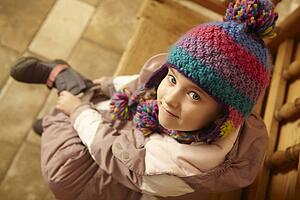 Young Girl Sitting On Wooden Seat Putting On Warm Outdoor Clothes And Boots