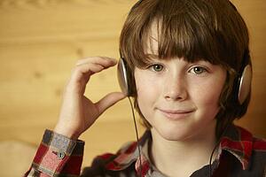 Young Boy Sitting On Wooden Seat Listening To MP3 Player