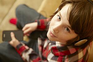 Young Boy Sitting On Wooden Seat Listening To MP3 Player